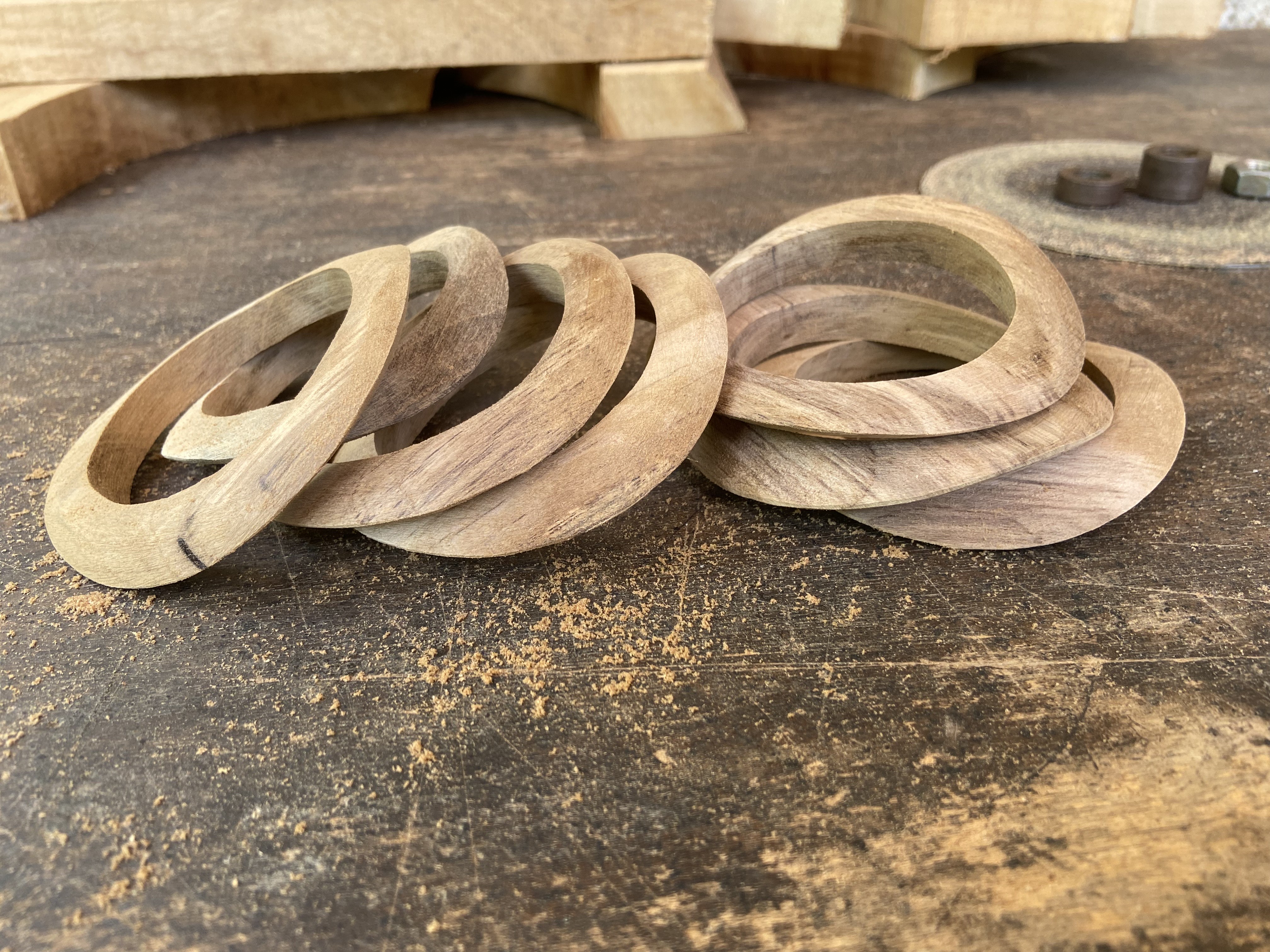 Rough-carved wooden bangles piled on a sawdust-covered workbench